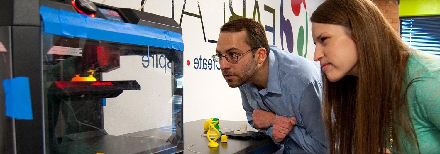 Two students watching a 3D printer in the FabLab